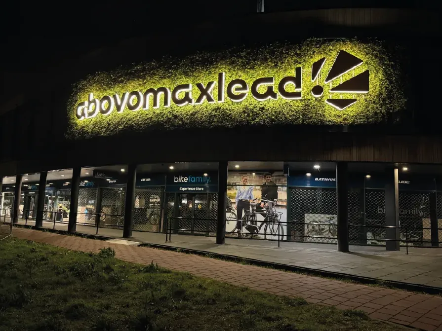 Verlichte letters en logo van Abovomaxlead op de groene plantenwand boven de winkelpuien